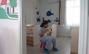 A nurse holds a newborn baby and feeds it in a room with baby cribs